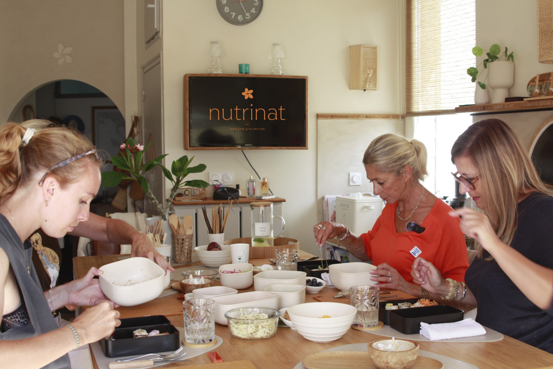Atelier culinaire nutrinat : préparation de bols équilibrés à plusieurs autour de la table de la Casa nutrinat, logo nutrinat affiché sur l'écran