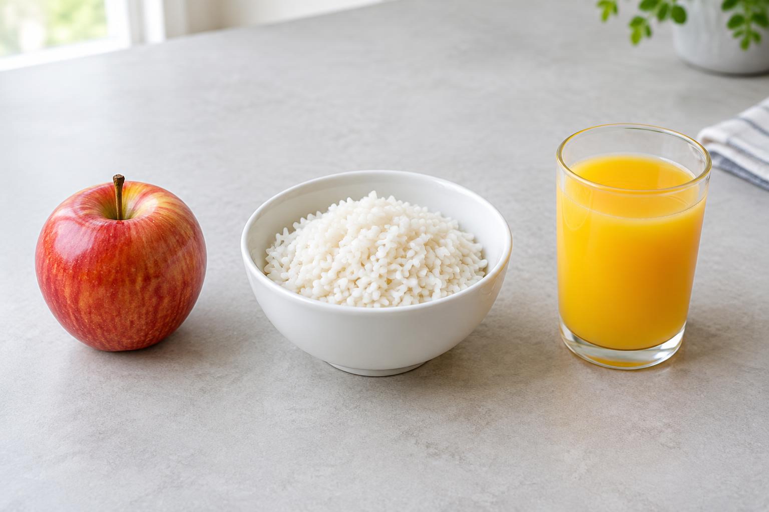 Une pomme rouge entière, un bol de riz cuit et un verre de jus d’orange sur une table